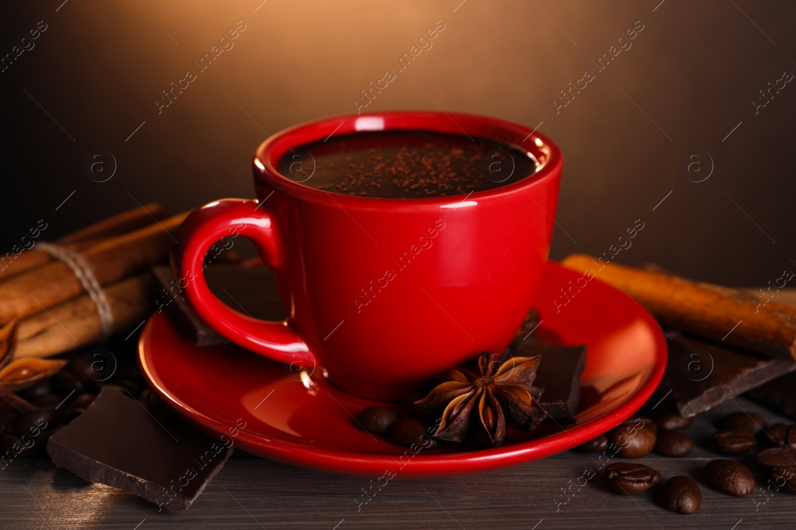 Photo of Cup of delicious hot chocolate, spices and coffee beans on wooden table