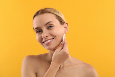 Photo of Smiling woman removing makeup with cotton pad on yellow background