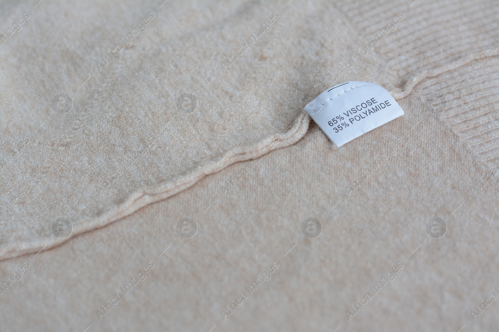 Photo of White clothing label with care information on beige garment, space for text
