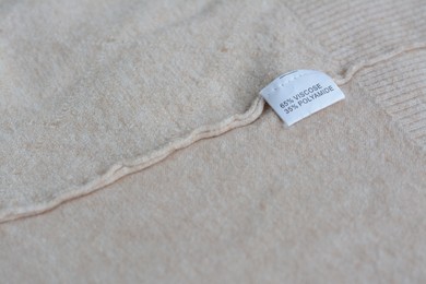 White clothing label with care information on beige garment, space for text