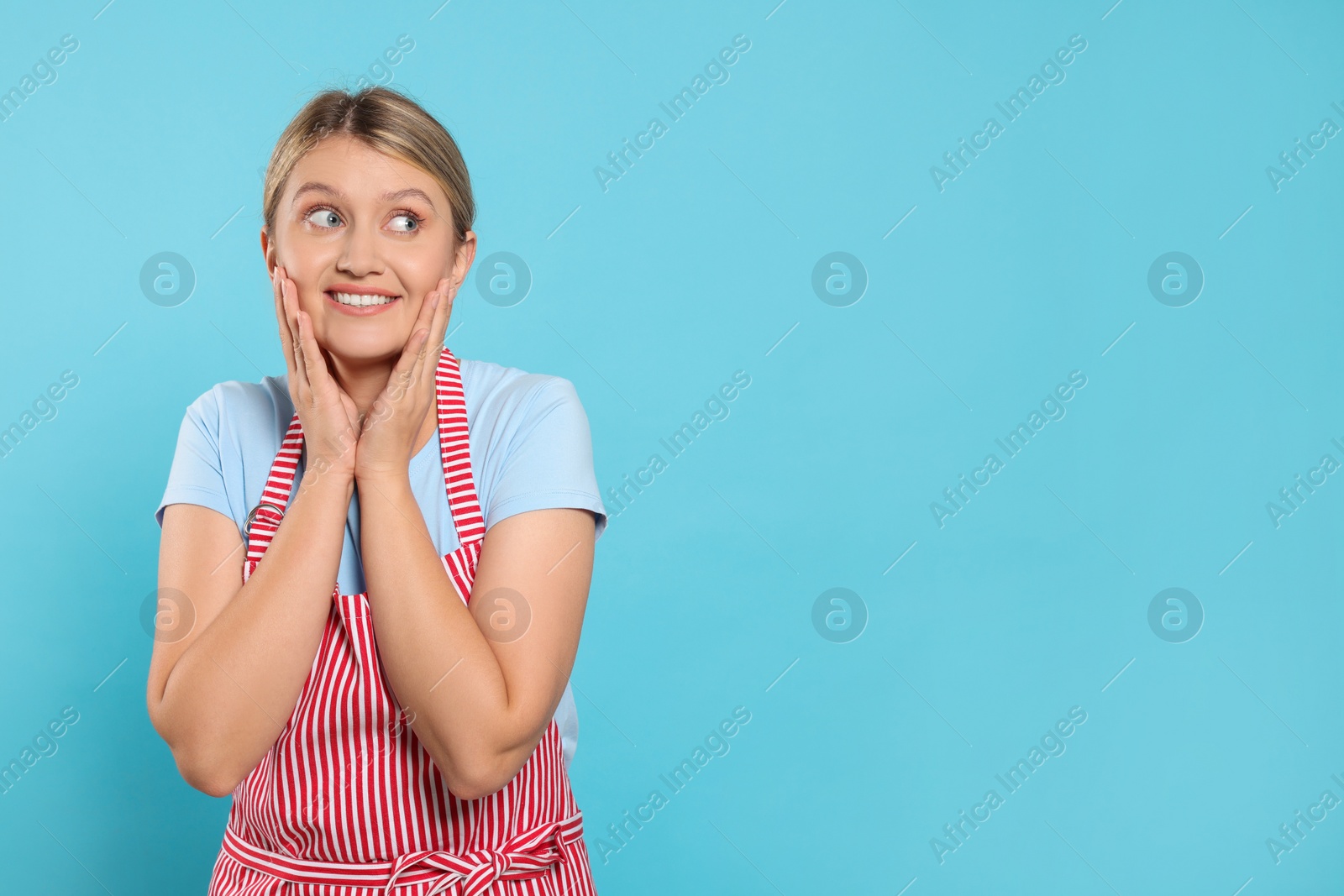 Photo of Beautiful young woman in clean striped apron on light blue background. Space for text