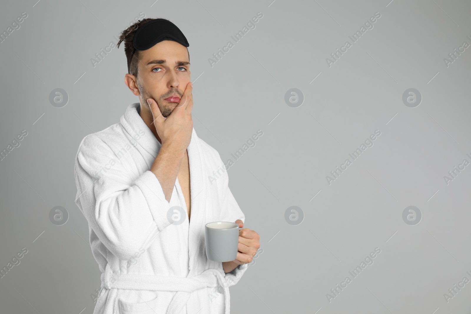Photo of Sleepy young man in bathrobe on light grey background. Space for text