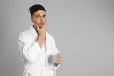 Sleepy young man in bathrobe on light grey background. Space for text