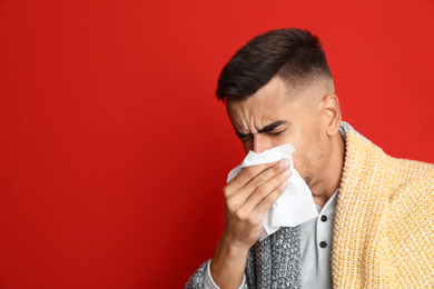 Man sneezing on red background, space for text. Cold symptoms