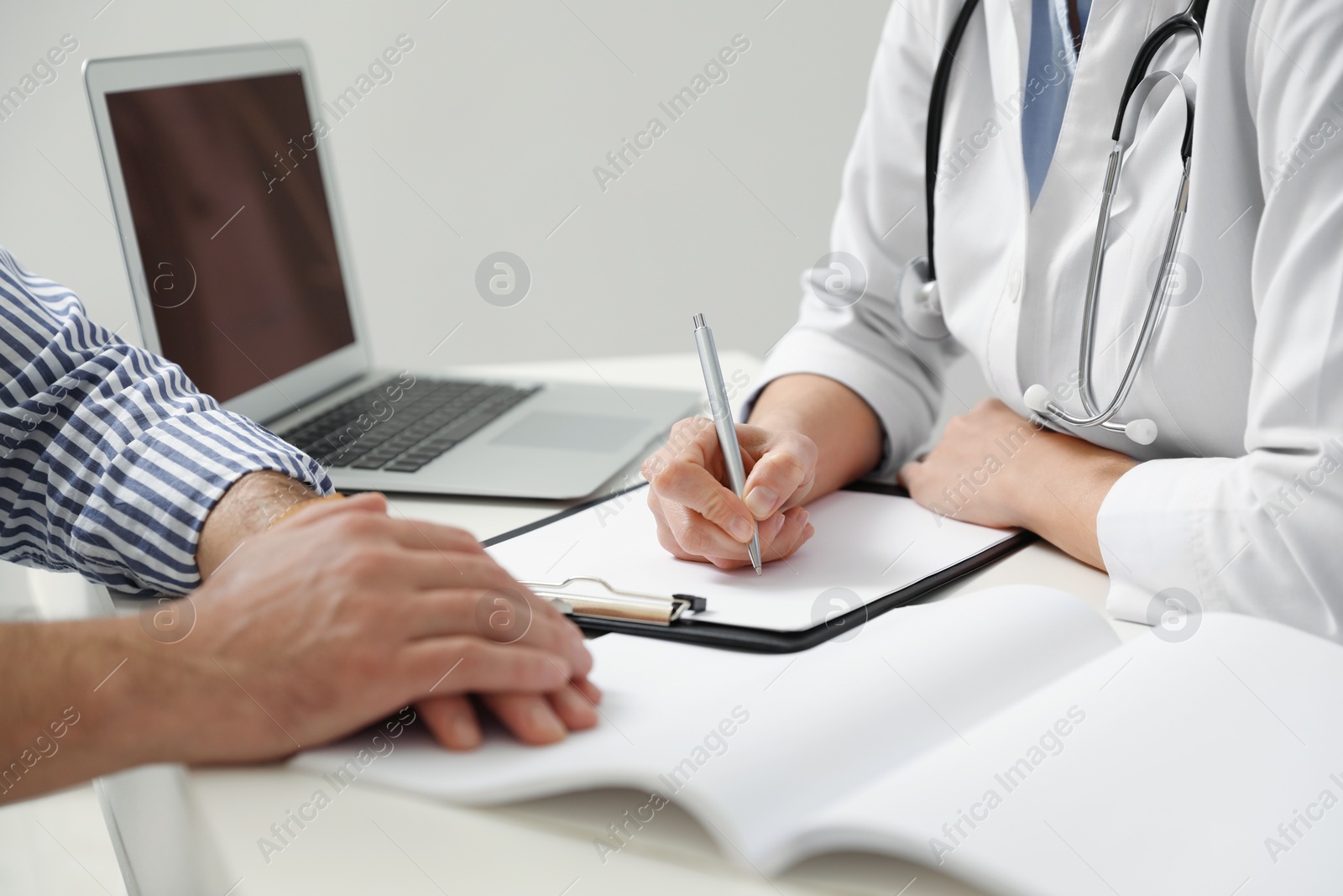 Photo of Doctor consulting patient at white table indoors, closeup