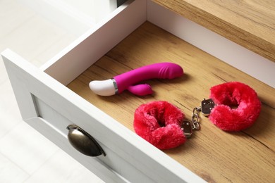 Photo of Fluffy handcuffs and vibrator in open wooden drawer. Sex toys