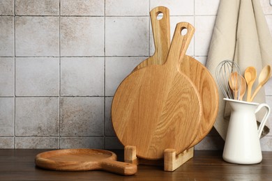 Photo of Wooden cutting boards and kitchen utensils on table near tiled wall. Space for text