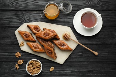 Delicious sweet baklava with walnuts, honey and hot tea on black wooden table, flat lay