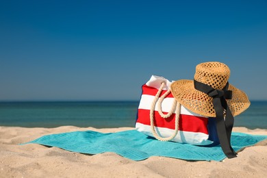 Photo of Turquoise beach towel with hat and bag on sand near sea, space for text