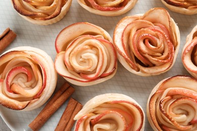 Photo of Freshly baked apple roses and cinnamon sticks on plate, flat lay. Beautiful dessert