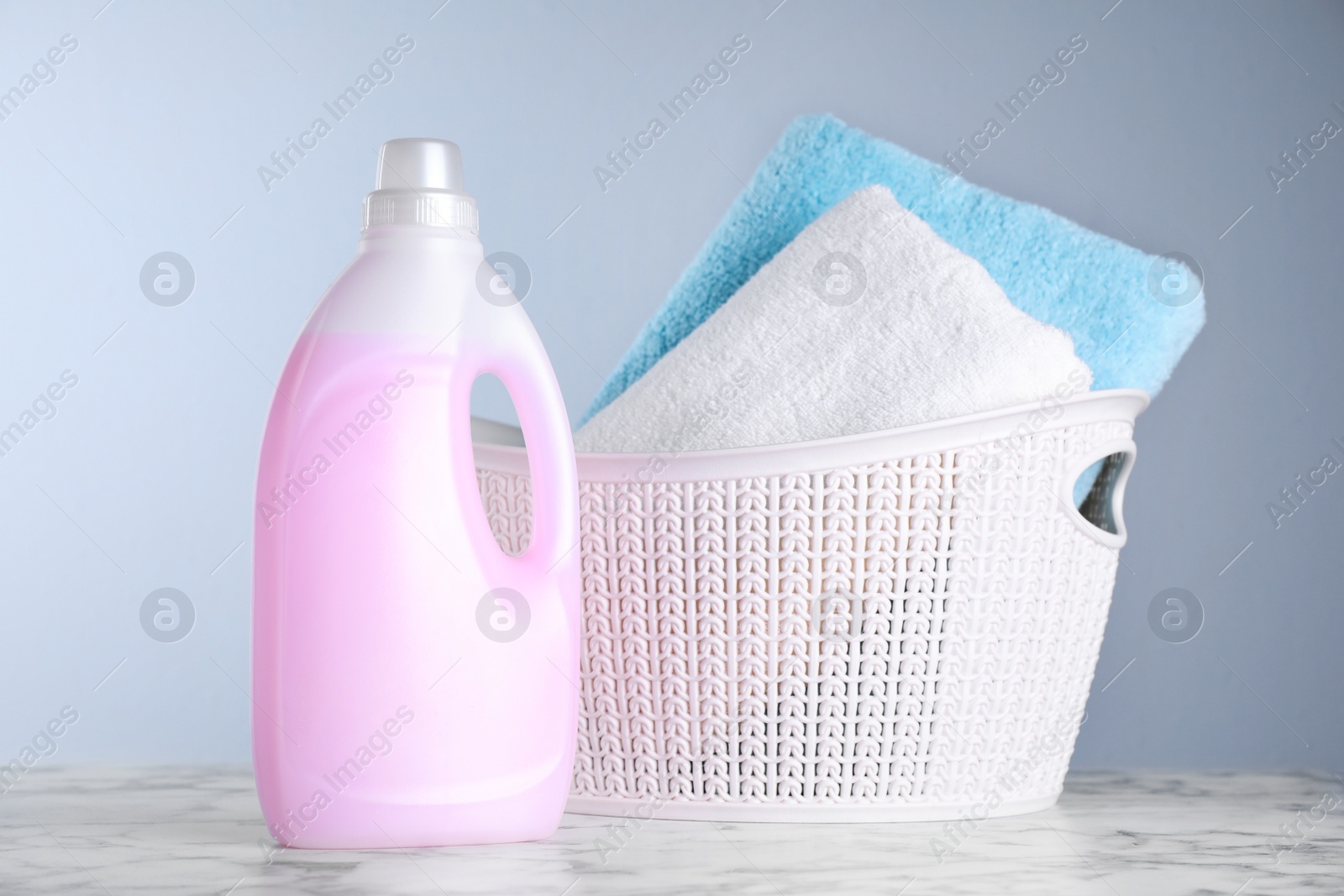 Photo of Bottle of laundry detergent and basket with towels on table