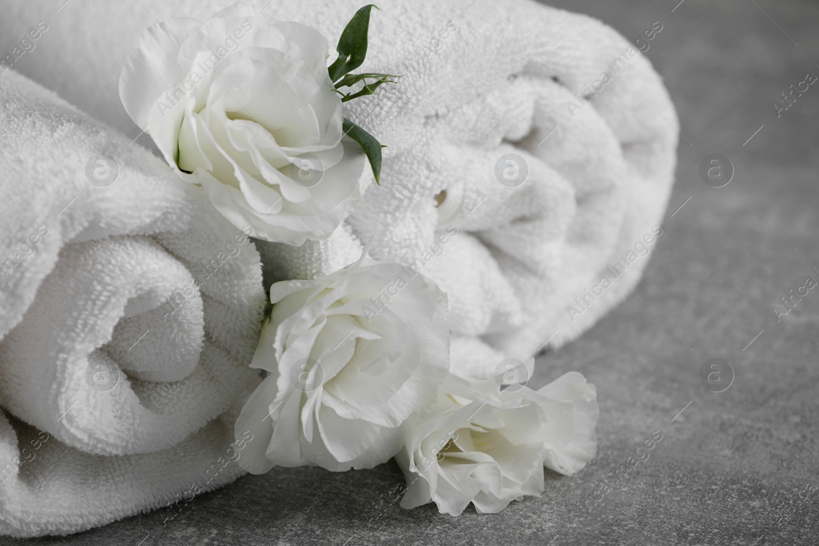Photo of White soft towels with flowers on grey table, closeup