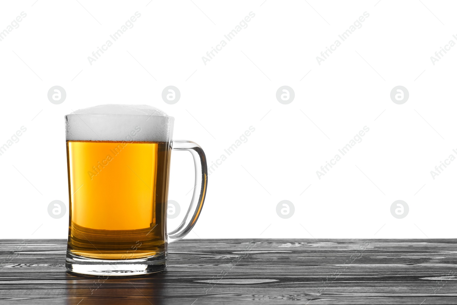 Photo of Glass mug of tasty beer on black wooden table against white background