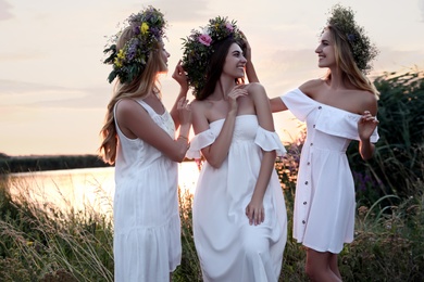 Young women wearing wreaths made of beautiful flowers outdoors at sunset