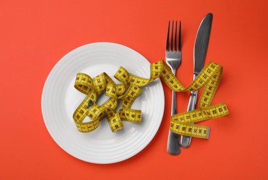 Photo of Plate, cutlery and measuring tape on red background, flat lay. Diet concept