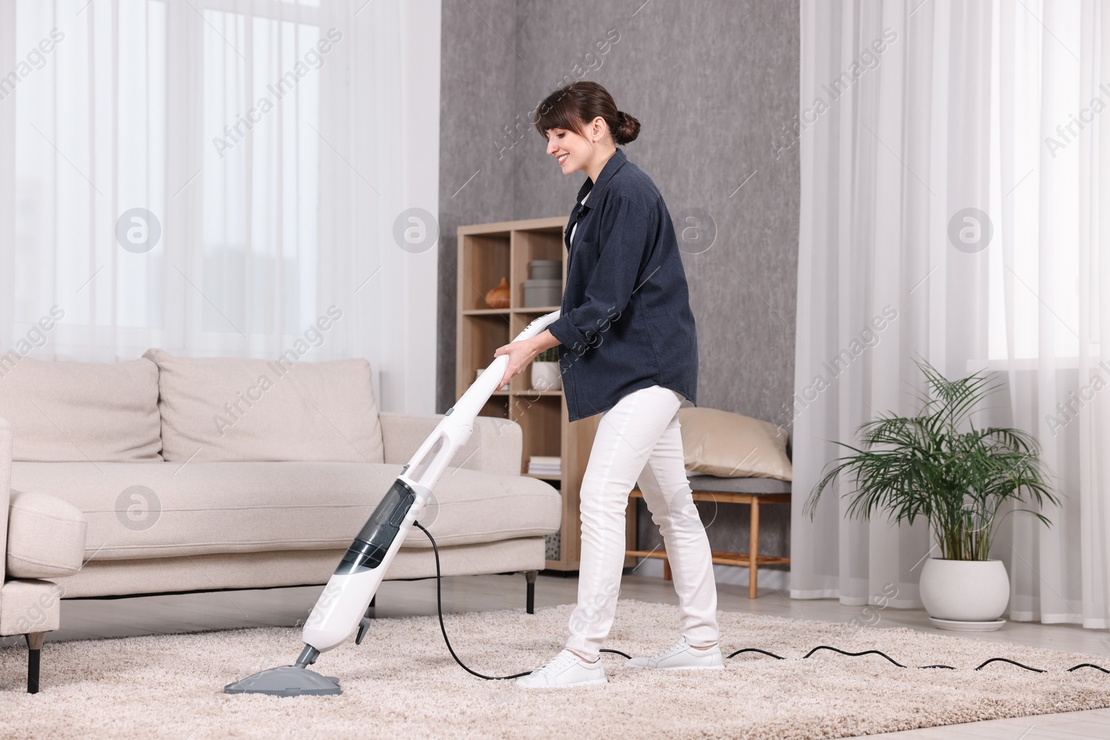 Photo of Happy young housewife vacuuming carpet at home