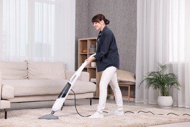 Happy young housewife vacuuming carpet at home