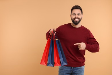 Photo of Smiling man pointing at many paper shopping bags on beige background. Space for text