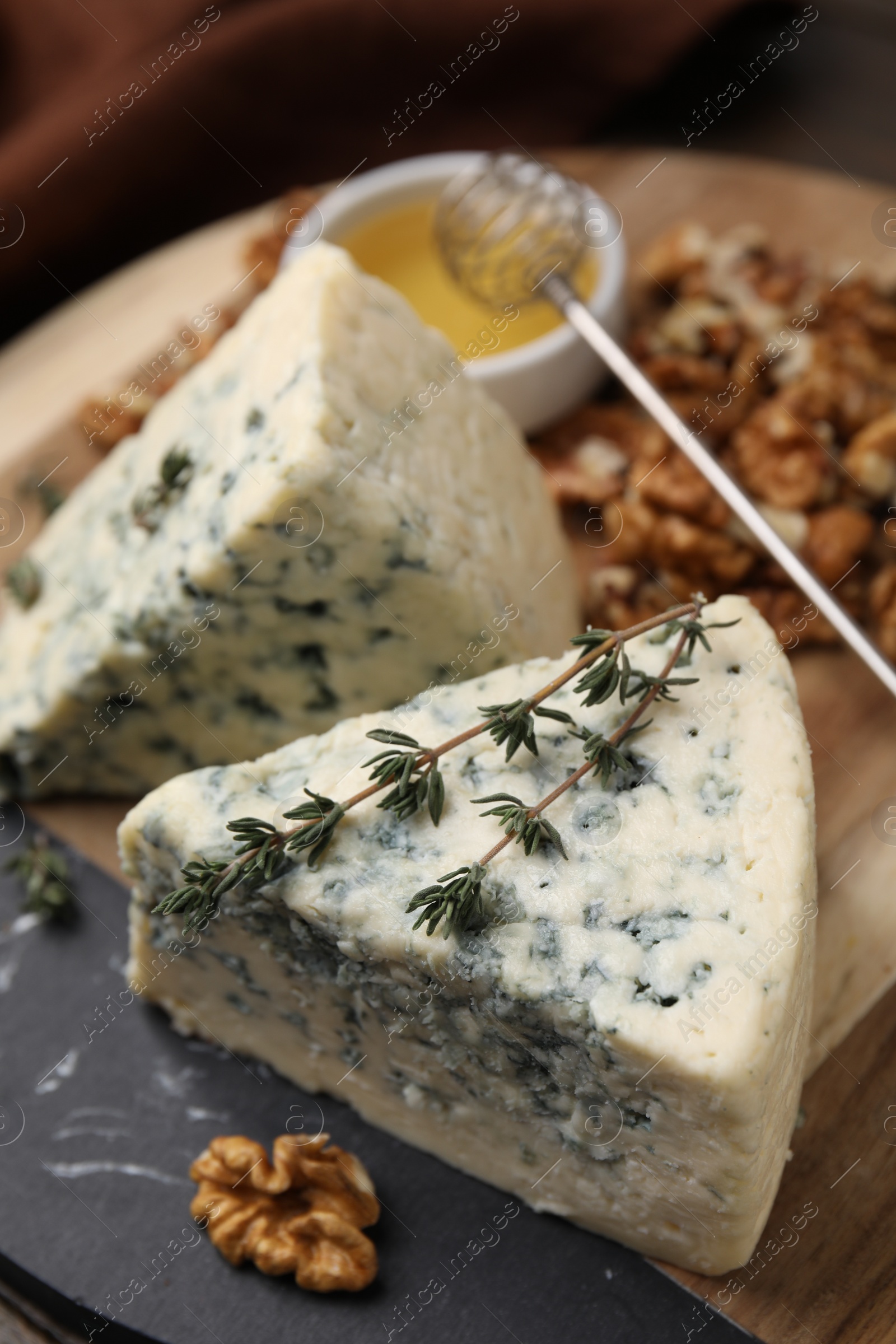 Photo of Tasty blue cheese with thyme, honey and walnuts on wooden board, closeup