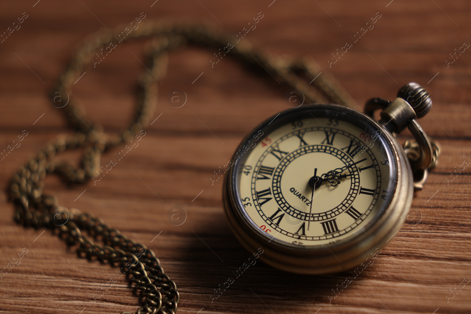 Photo of Pocket clock with chain on wooden table, closeup