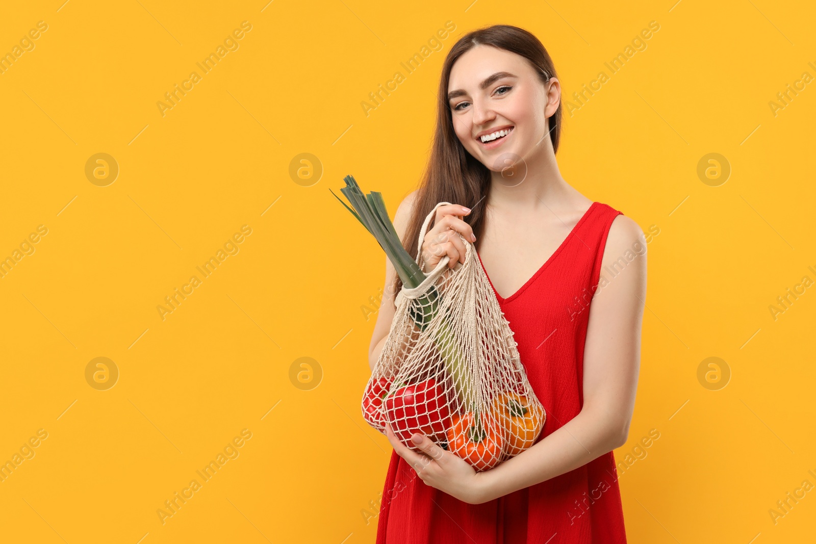 Photo of Woman with string bag of fresh vegetables on orange background, space for text