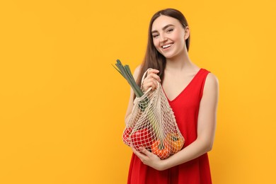 Woman with string bag of fresh vegetables on orange background, space for text
