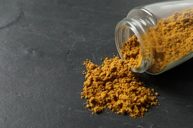 Jar with dry curry powder on dark textured table, closeup. Space for text