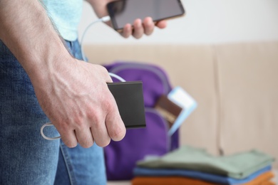 Man charging mobile phone with power bank while getting ready for travel, closeup