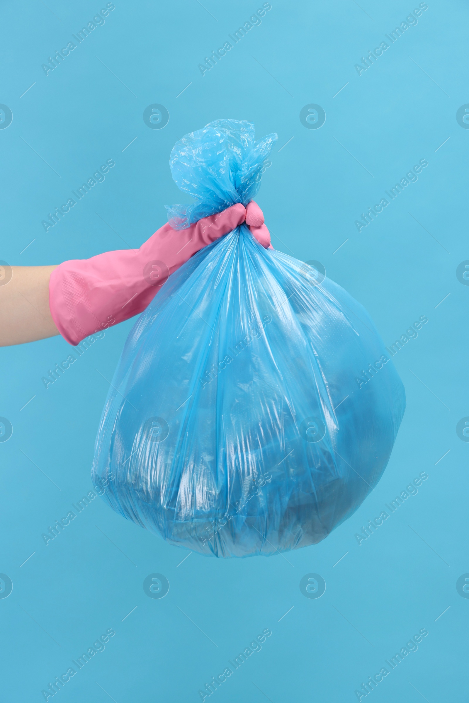 Photo of Woman holding plastic bag full of garbage on light blue background, closeup