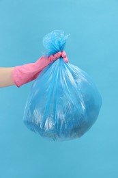 Photo of Woman holding plastic bag full of garbage on light blue background, closeup