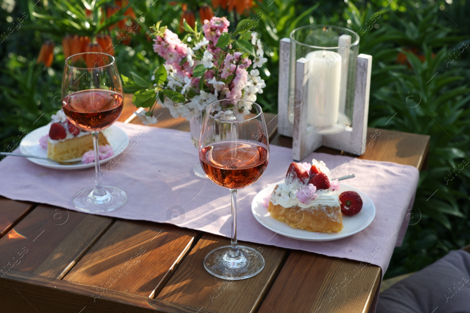 Photo of Vase with spring flowers, wine and cake on table served for romantic date in garden