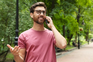 Handsome man talking on smartphone in park, space for text