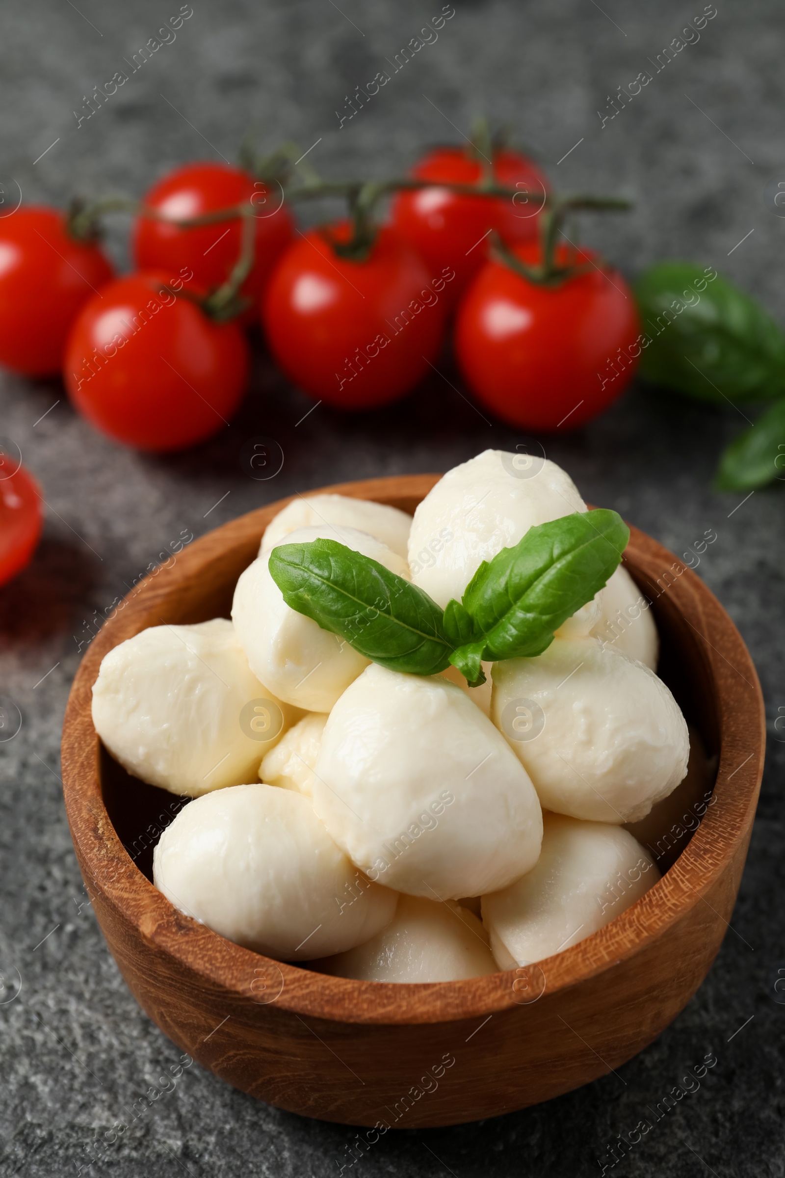 Photo of Delicious mozzarella balls in wooden bowl and basil leaves on light gray table, closeup