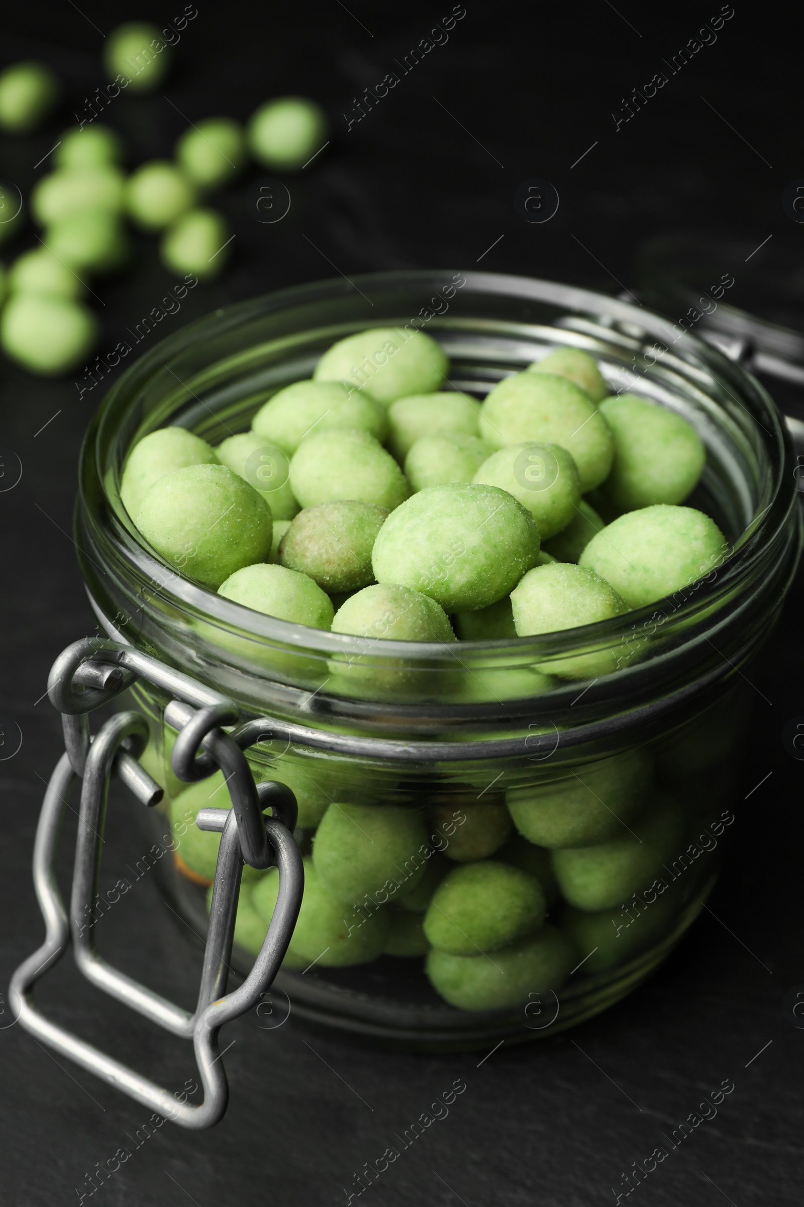 Photo of Tasty wasabi coated peanuts in glass jar on black table, closeup