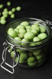 Tasty wasabi coated peanuts in glass jar on black table, closeup