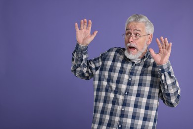 Portrait of surprised senior man on violet background, space for text