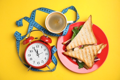 Photo of Flat lay composition with tasty sandwiches and alarm clock on yellow background. Nutrition regime