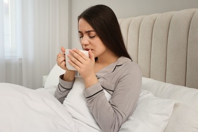 Sick young woman with cup of hot drink in bed at home