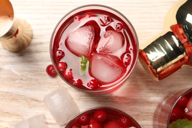 Tasty cranberry cocktail with ice cubes in glasses and bartender's tools on wooden table, flat lay