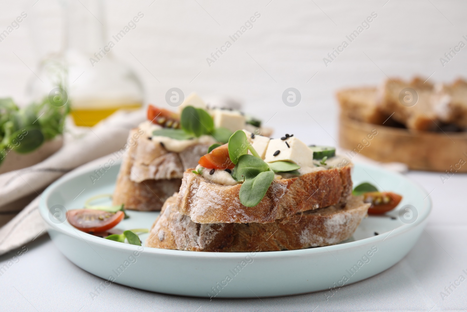 Photo of Tasty vegan sandwiches with tofu, cucumber, tomato and sesame seeds on white tiled table