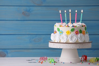 Photo of Delicious birthday cake and party decor on white wooden table against light blue background, space for text