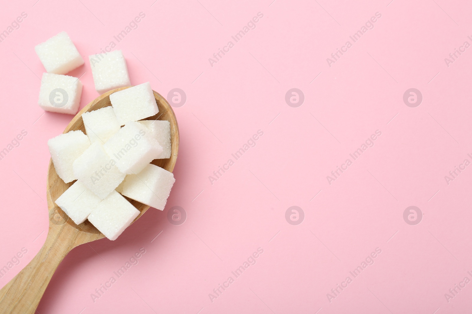 Photo of White sugar cubes in wooden spoon on pink background, top view. Space for text