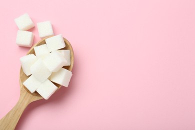 Photo of White sugar cubes in wooden spoon on pink background, top view. Space for text