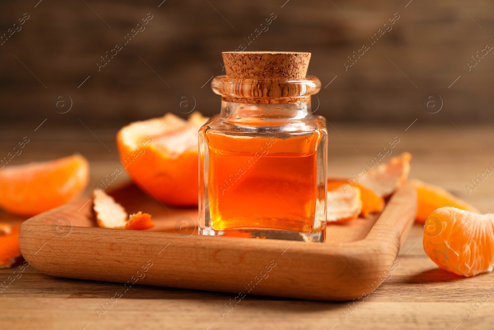 Photo of Bottle of tangerine essential oil and peeled fresh fruit on wooden table, closeup