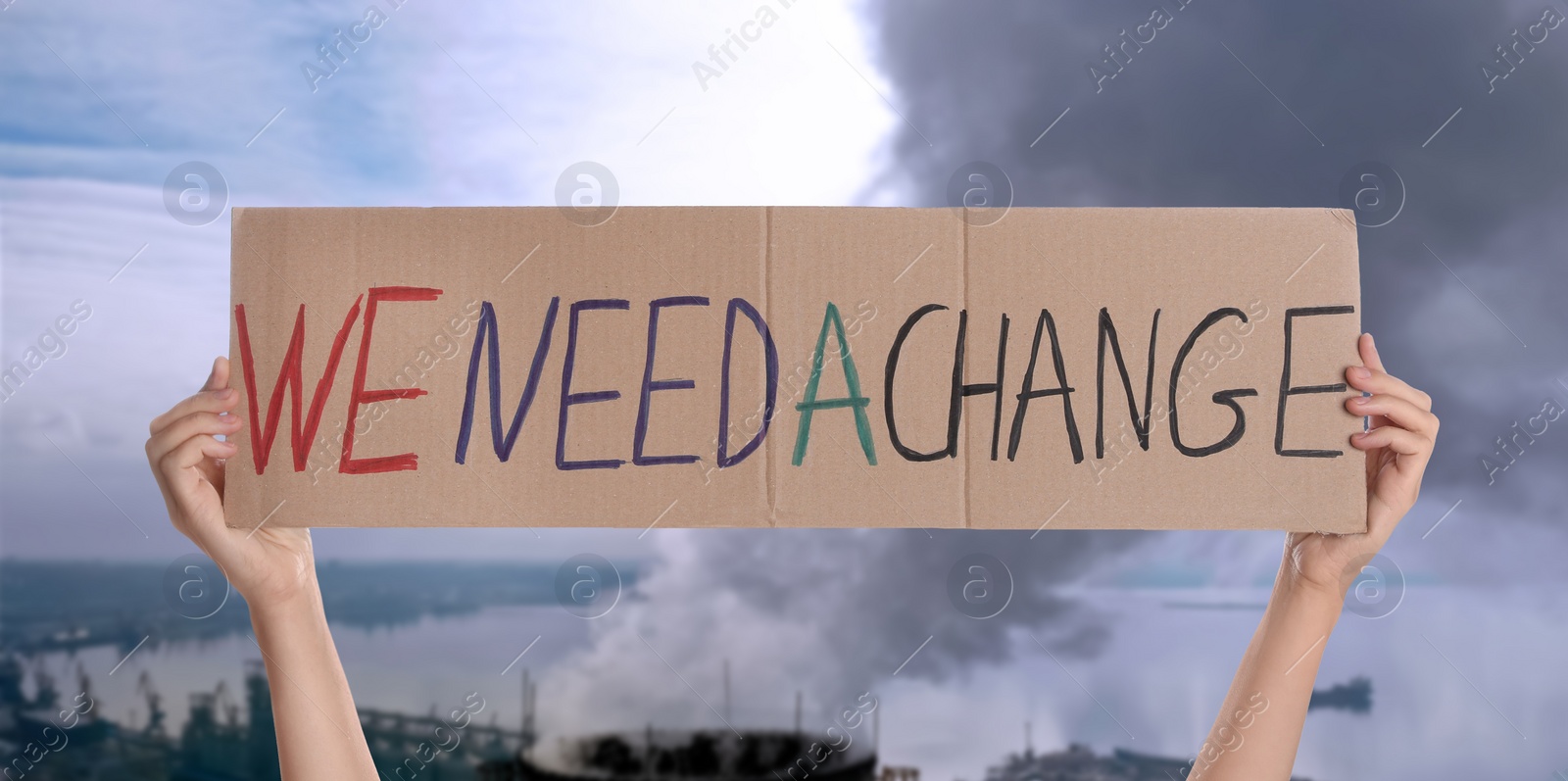 Image of Protestor holding placard with text We Need A Change and blurred view of industrial factory on background. Climate strike