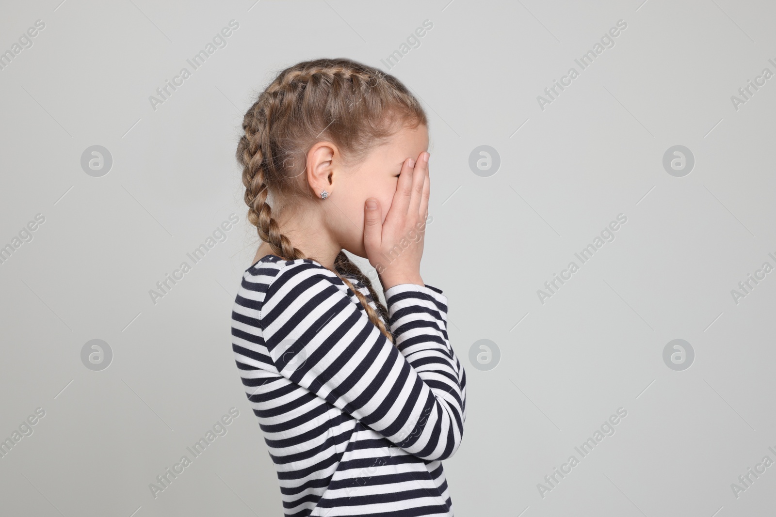 Photo of Girl covering face with hands on light grey background. Children's bullying