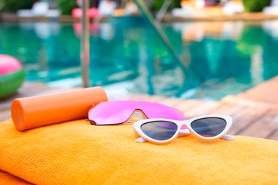 Sunglasses and sunscreen on beach towel near outdoor swimming pool, closeup. Luxury resort