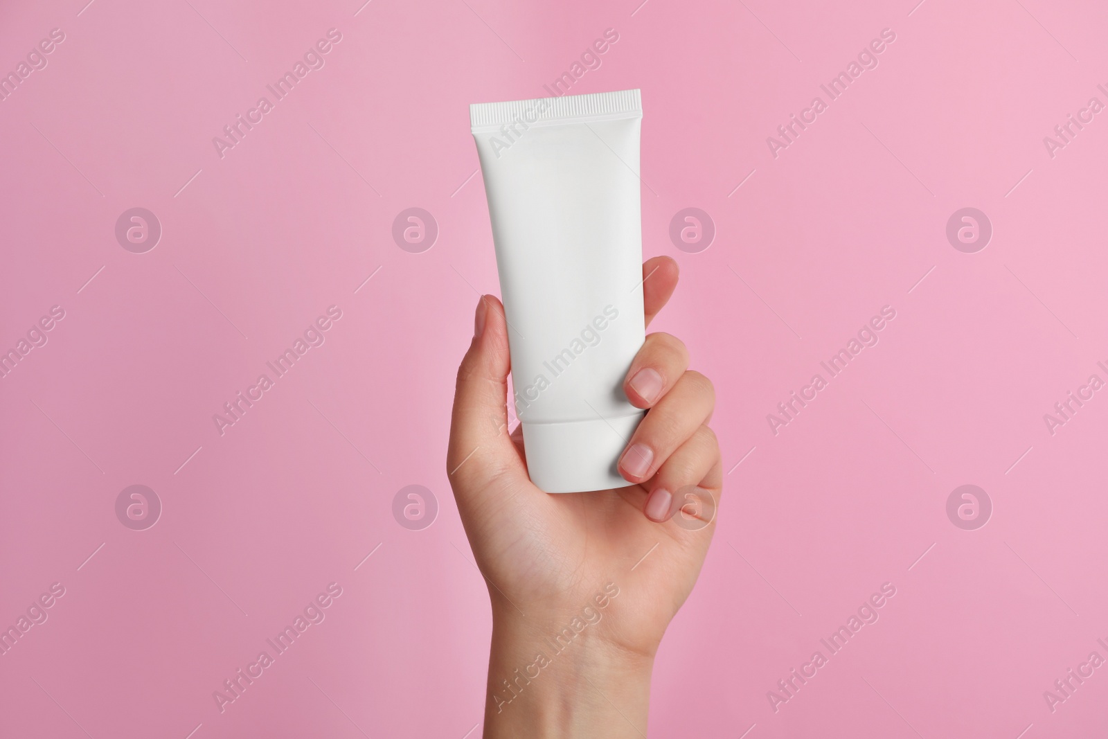 Photo of Woman holding tube of face cream on pink background, closeup