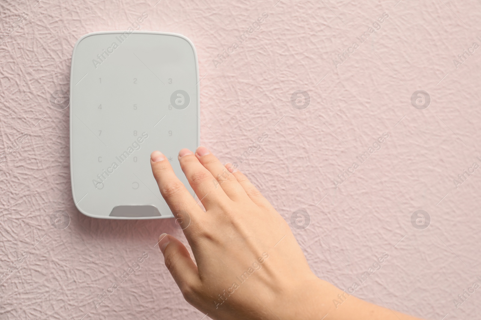 Photo of Young woman entering code on alarm system keypad indoors