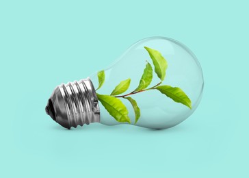 Image of Saving energy, eco-friendly lifestyle. Fresh green leaves inside of light bulb on turquoise background